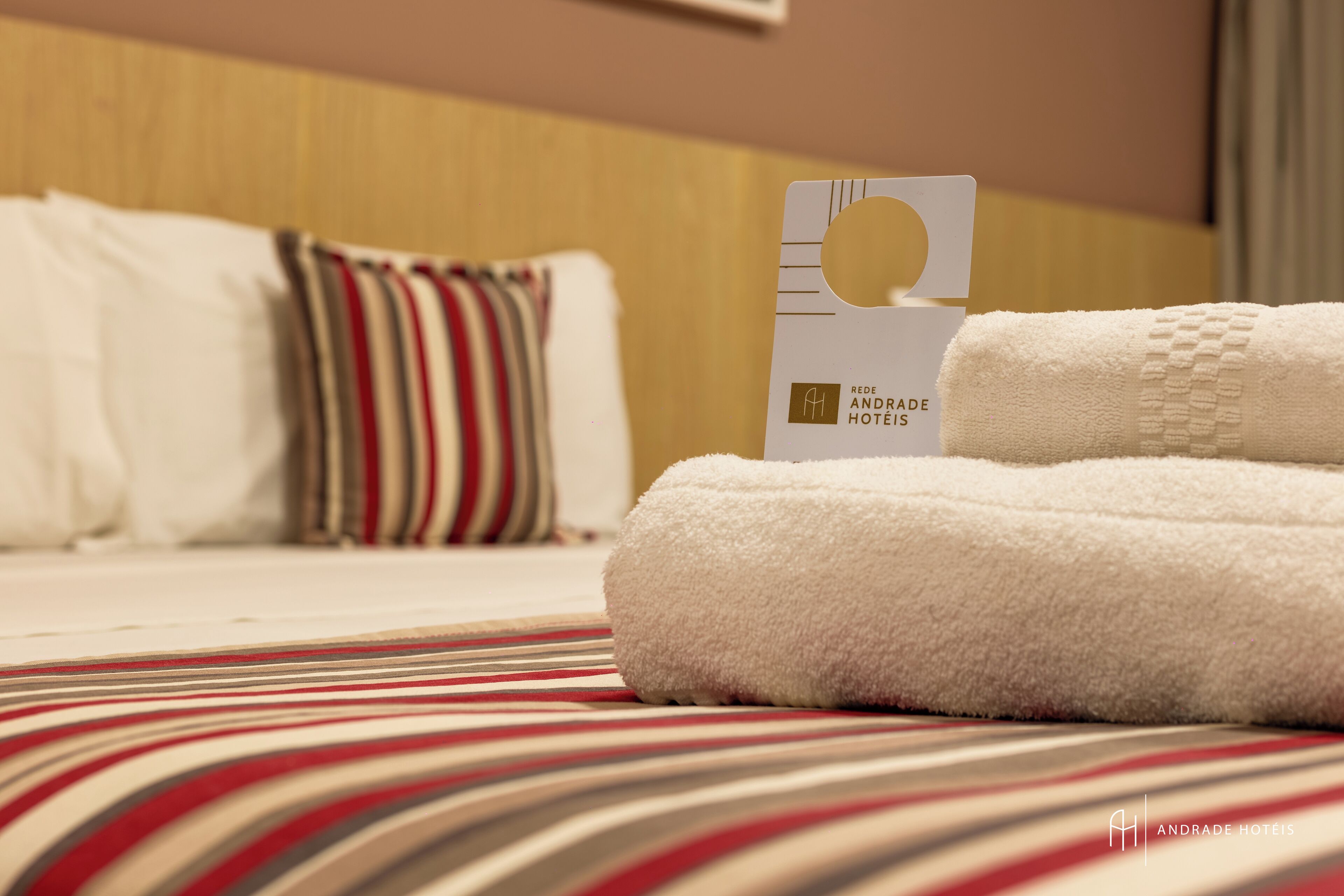 A neatly made bed with striped bedding, a white towel, and a hotel card on the bed.