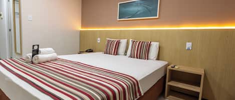 Una habitación de hotel con una cama grande, ropa de cama a rayas, una mesita de noche y un cuadro en la pared, además de una puerta.