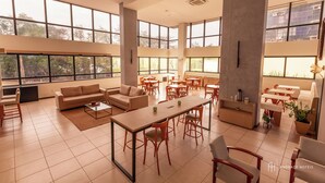 A spacious hotel lobby with high ceilings, large windows, and a mix of seating arrangements including sofas, chairs, and tables. - Rede Andrade SLZ (São Luís)
