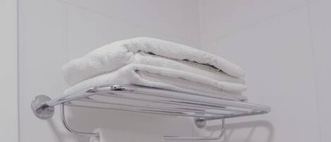 A bathroom with white tiled walls, a towel rack with folded towels, and a visible light switch.