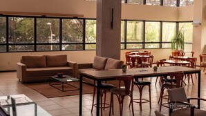 A spacious indoor area with large windows, a sofa, dining tables, and chairs. - Rede Andrade SLZ (São Luís)