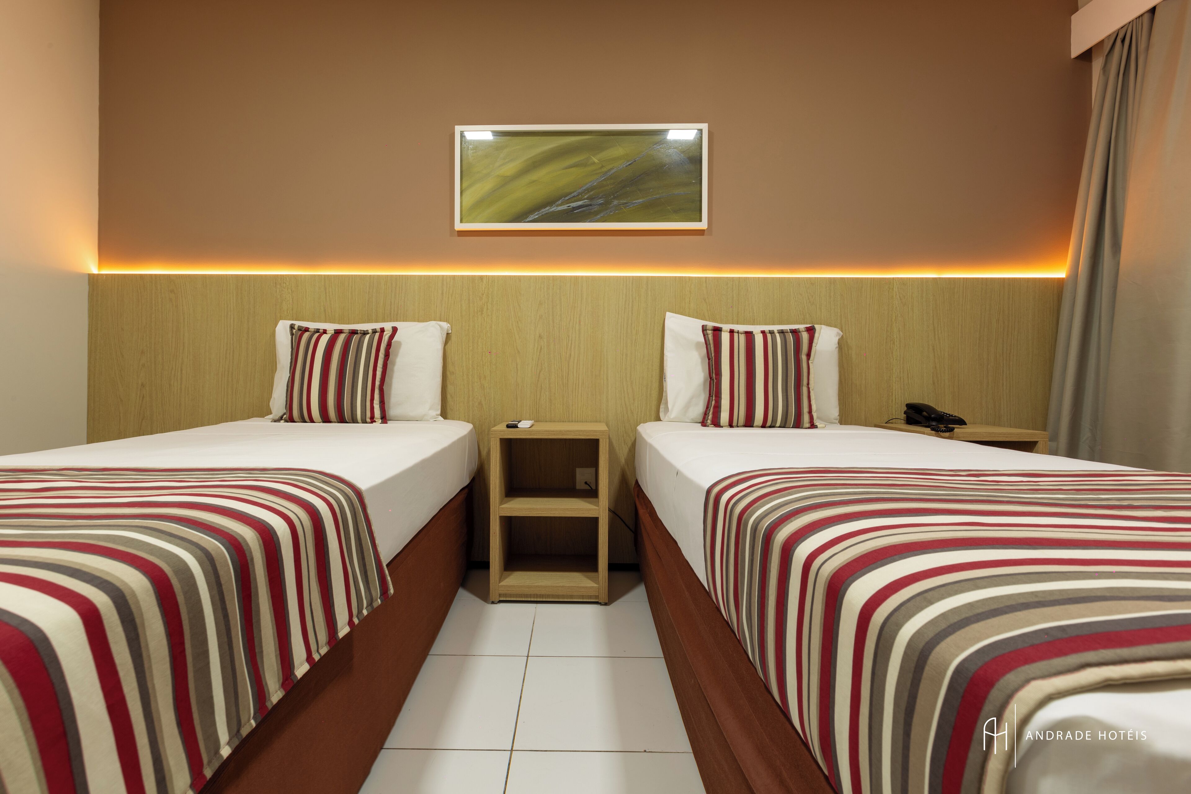A hotel room with two beds, a nightstand, a small shelf, and a painting on the wall.