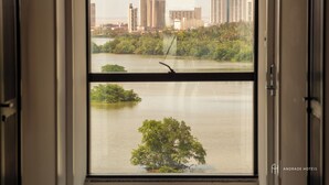 A view through a window with a cityscape in the background, including high-rise buildings and a body of water with greenery. - Rede Andrade SLZ (São Luís)