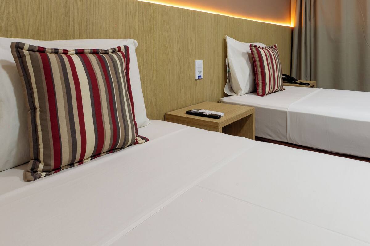 A hotel room with two beds, a nightstand with a remote control, a painting on the wall, and a curtain on the window.