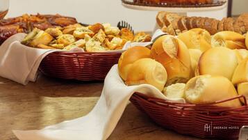 Uma mesa de buffet com diversos alimentos, incluindo pão, pães e um bolo.