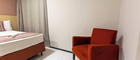 Ein Hotelzimmer mit einem Bett, einem roten Sessel und einem weißen Vorhang.