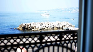 A rocky breakwater with boats, a clear sky, and a distant shoreline. - Partenope Relais (Naples)