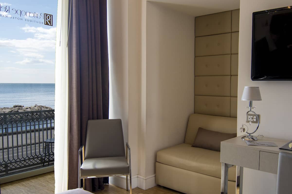 A hotel room with a bed, a desk with a lamp, a chair, a sofa, and a TV mounted on the wall.