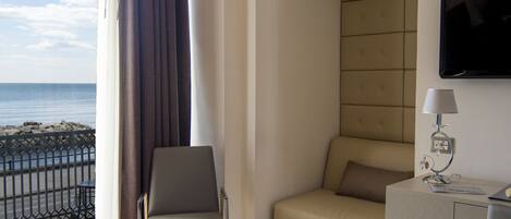 A hotel room with a bed, a desk with a lamp, a chair, a sofa, and a TV mounted on the wall.