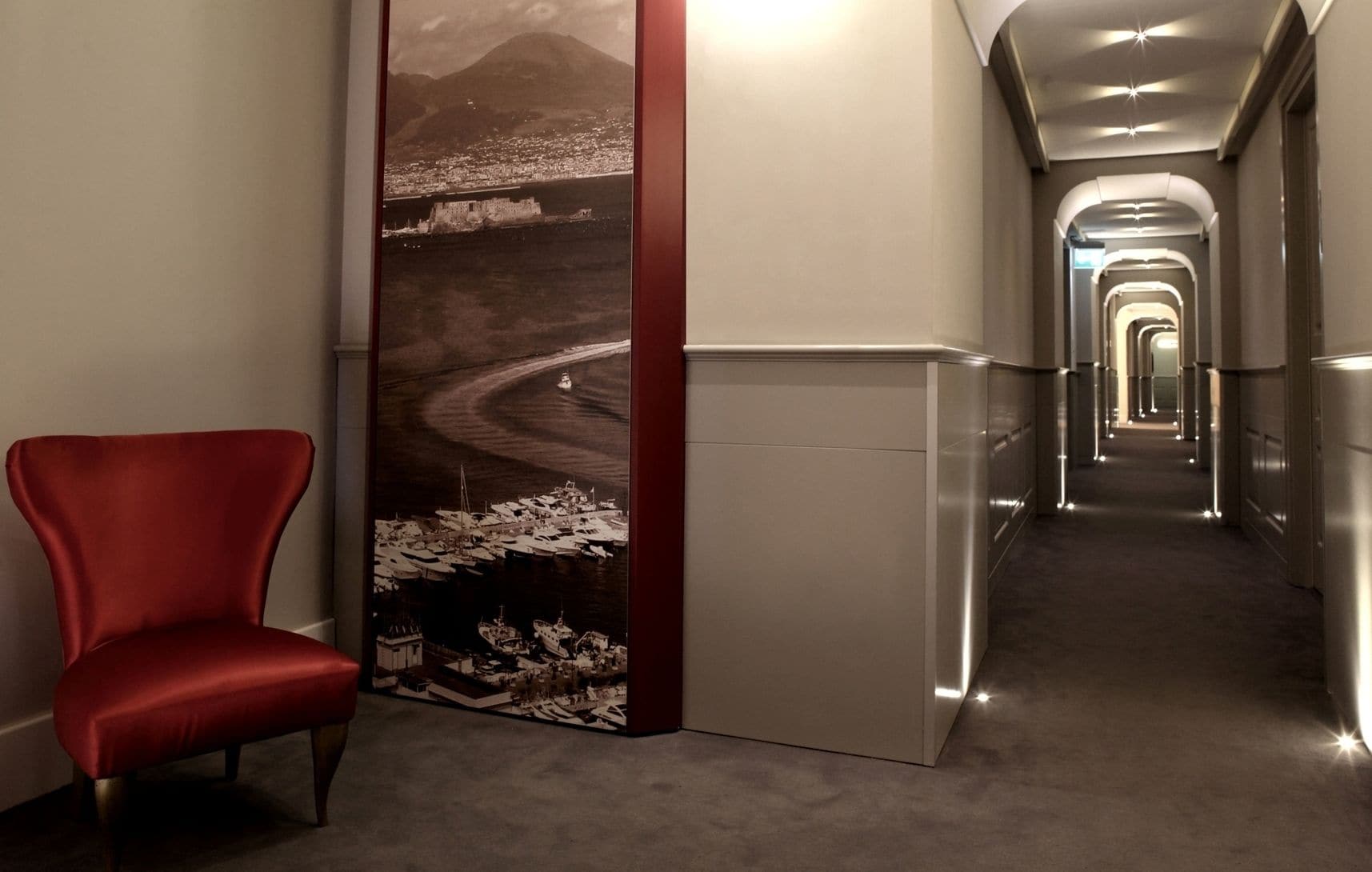 A hallway with a red chair, a large wall mural, and a long corridor with doors.