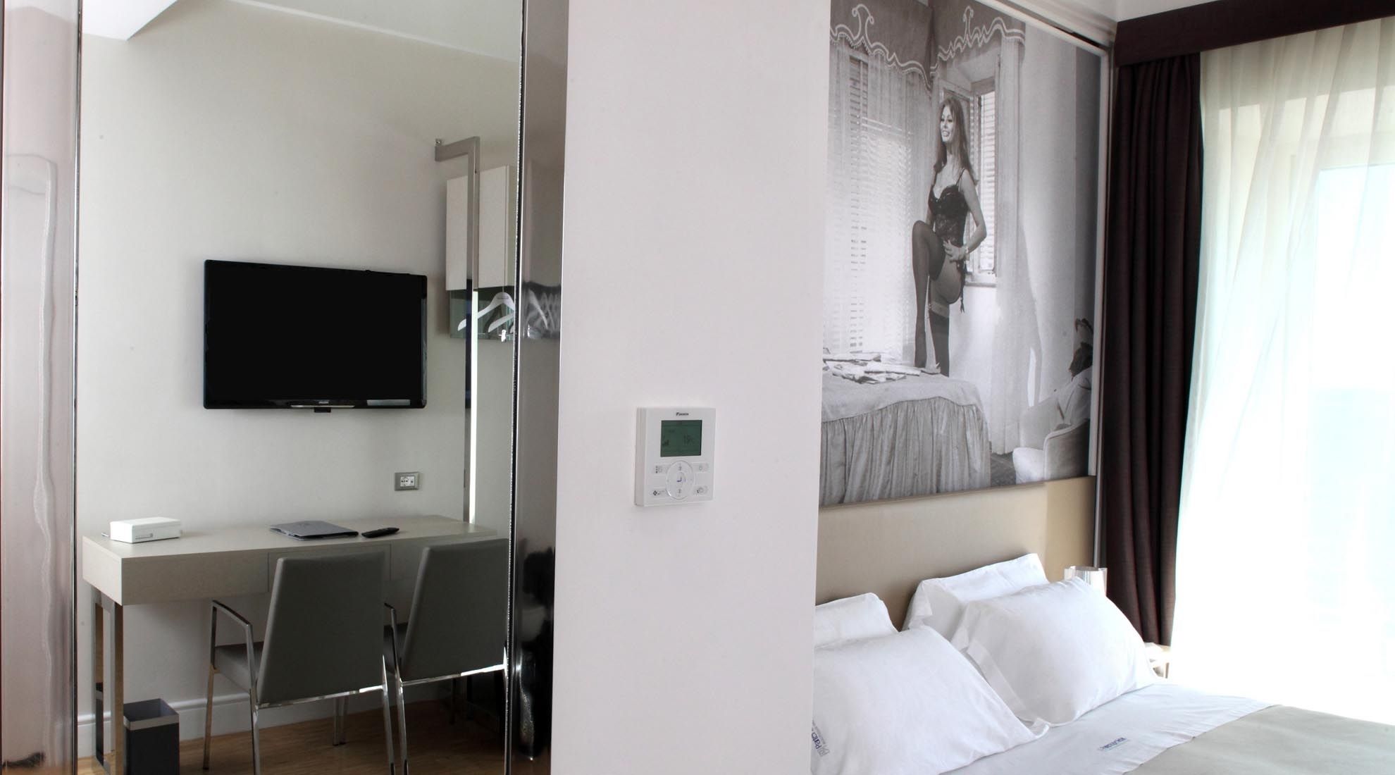 Une chambre d’hôtel équipée d’un lit, d’un bureau avec une chaise, d’une télévision et d’un thermostat.