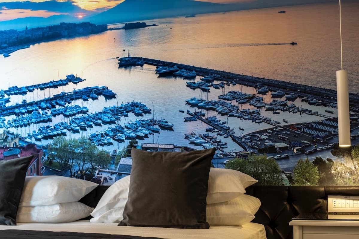 A bed with pillows and a view of a marina with boats.