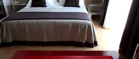 A hotel room with a bed, a red table, and a nightstand with a lamp.