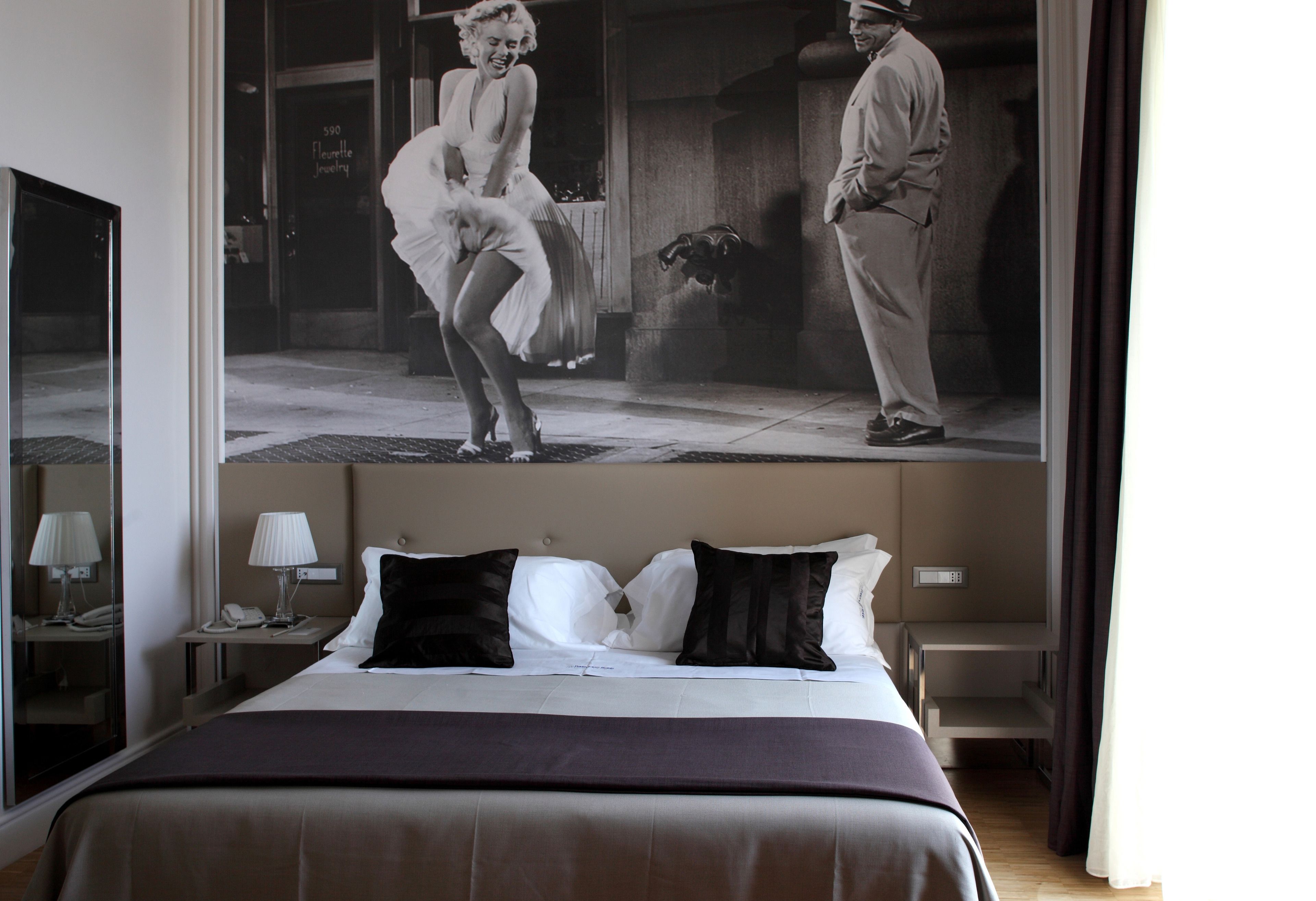 A hotel room with a large bed, a nightstand with a lamp, and a wall-mounted TV.