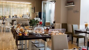 A hotel breakfast area with buffet tables, seating, and a kitchen visible in the background. - Partenope Relais (Naples)