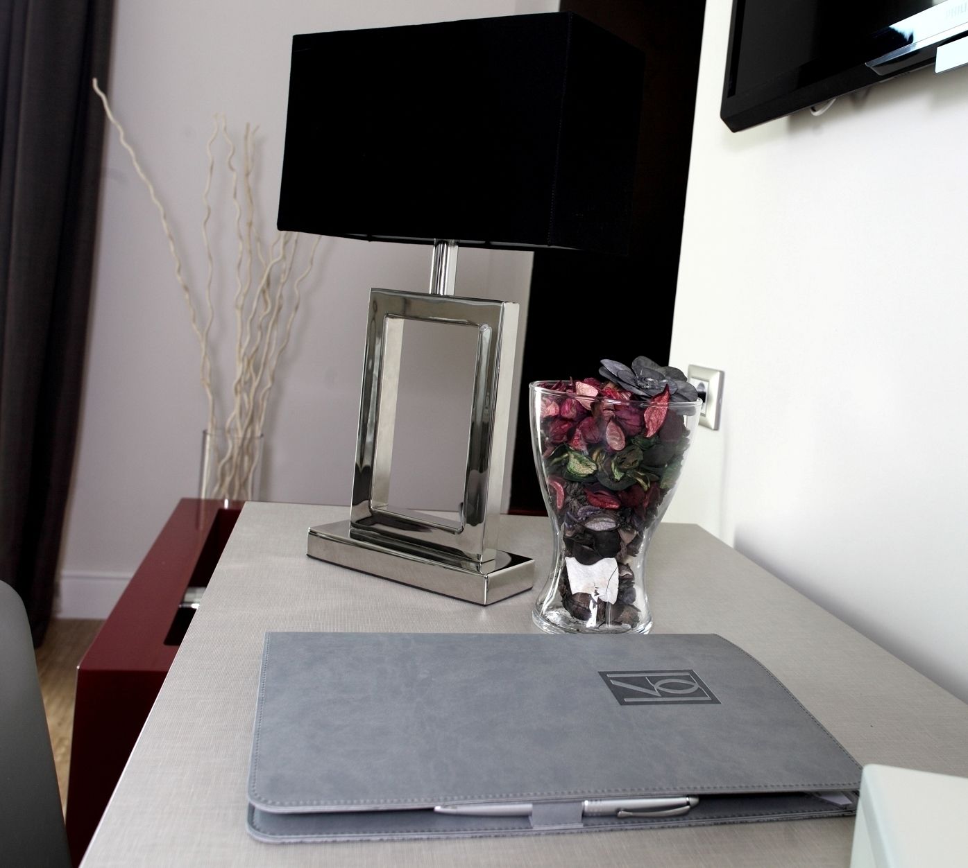 A laptop on a table with a clear glass vase containing dried flowers.