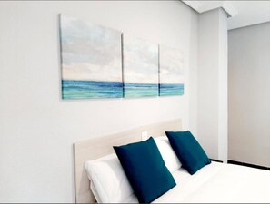 A hotel room with a bed, two pillows, and a wall with three paintings of the sea. - Hostal Lucía by gaiarooms (Salamanca)