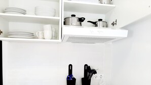 A kitchen with a stainless steel sink, white countertop, and a black and white induction cooktop. There are white shelves above the cooktop holding dishes and glasses. - Hostal Lucía by gaiarooms (Salamanca)