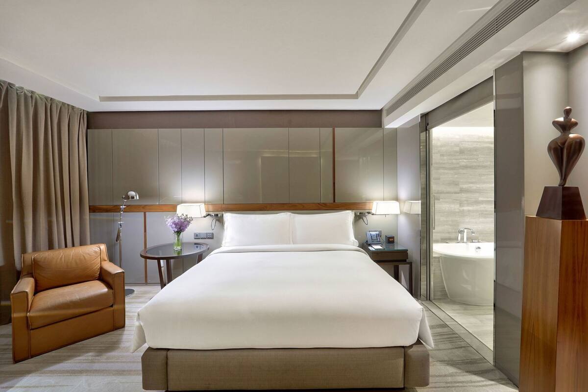 Une chambre d’hôtel avec un grand lit, un fauteuil en cuir, une table de chevet avec une lampe, un téléphone et un vase avec des fleurs.