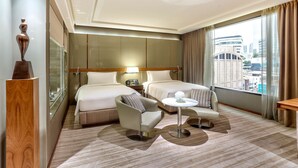 A hotel room with two beds, a sitting area with a table, and a view of the city. - Hilton Sukhumvit Bangkok (Bangkok)