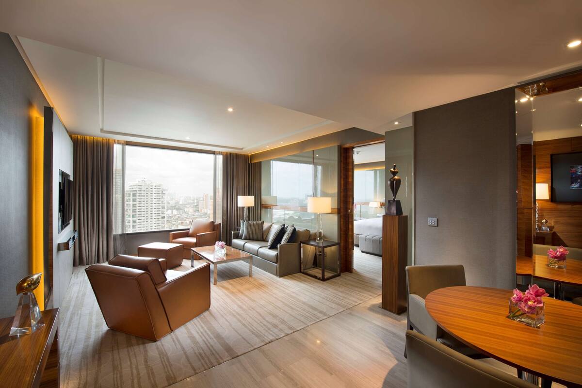 Une chambre d’hôtel moderne dotée d’un espace salon, d’une table à manger et d’une grande fenêtre donnant sur la ville.