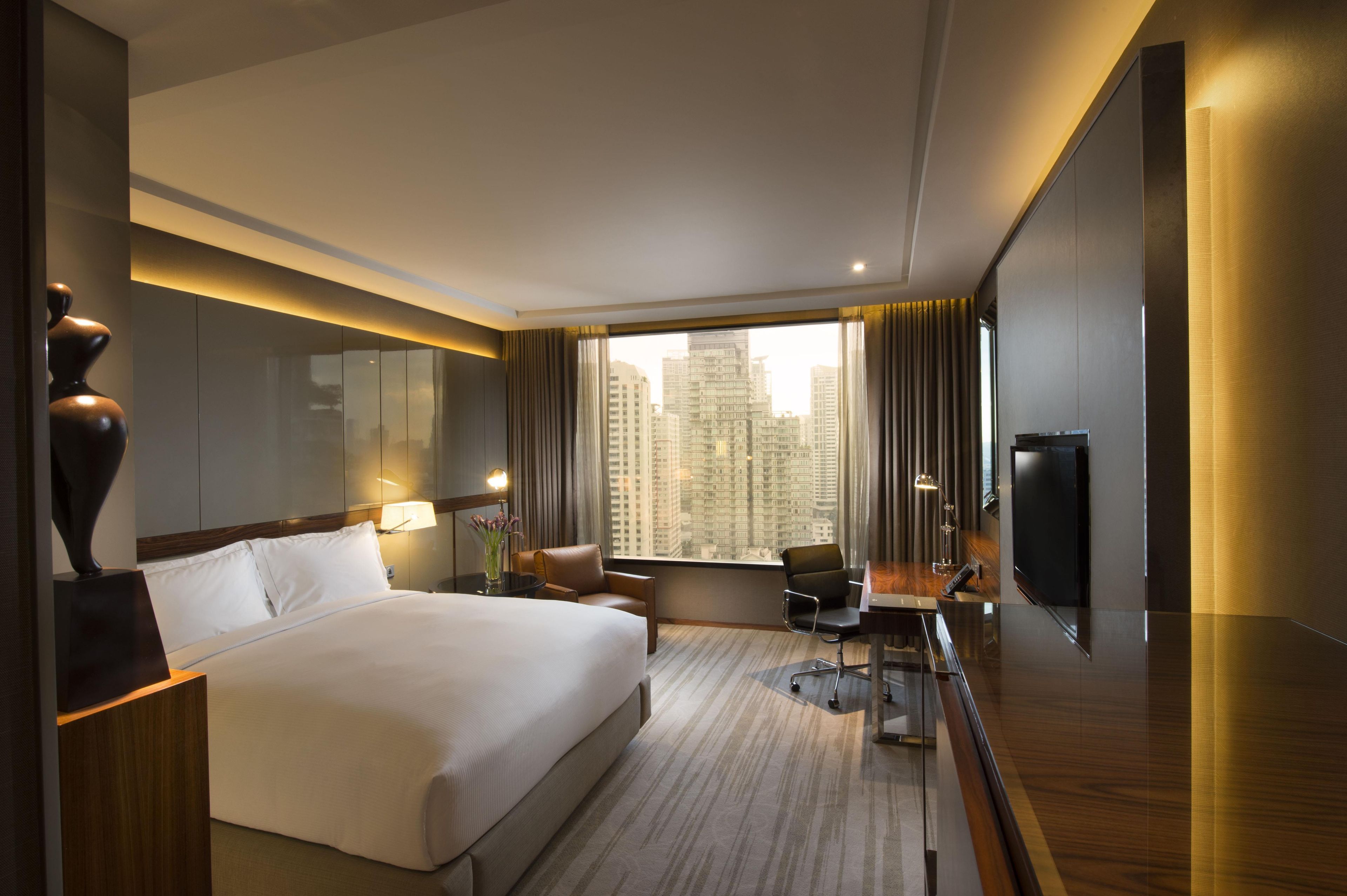 A hotel room with a large bed, a desk, a chair, a TV, and a view of the cityscape.
