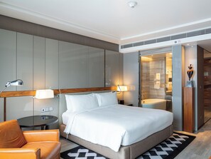 A modern hotel room with a bed, a seating area, a small table, and a bathroom visible through a glass door. - Hilton Sukhumvit Bangkok (Bangkok)
