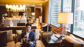 A man sitting on a sofa in a hotel lobby with a city view, a desk with a lamp, and a staircase.