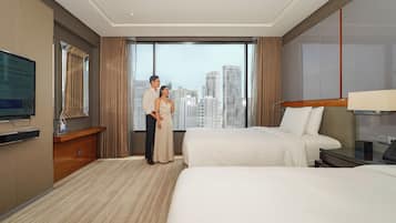 A hotel room with a large window, a bed, a desk, and a television.