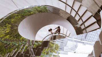 A spiral staircase with glass railings and a view of greenery below.