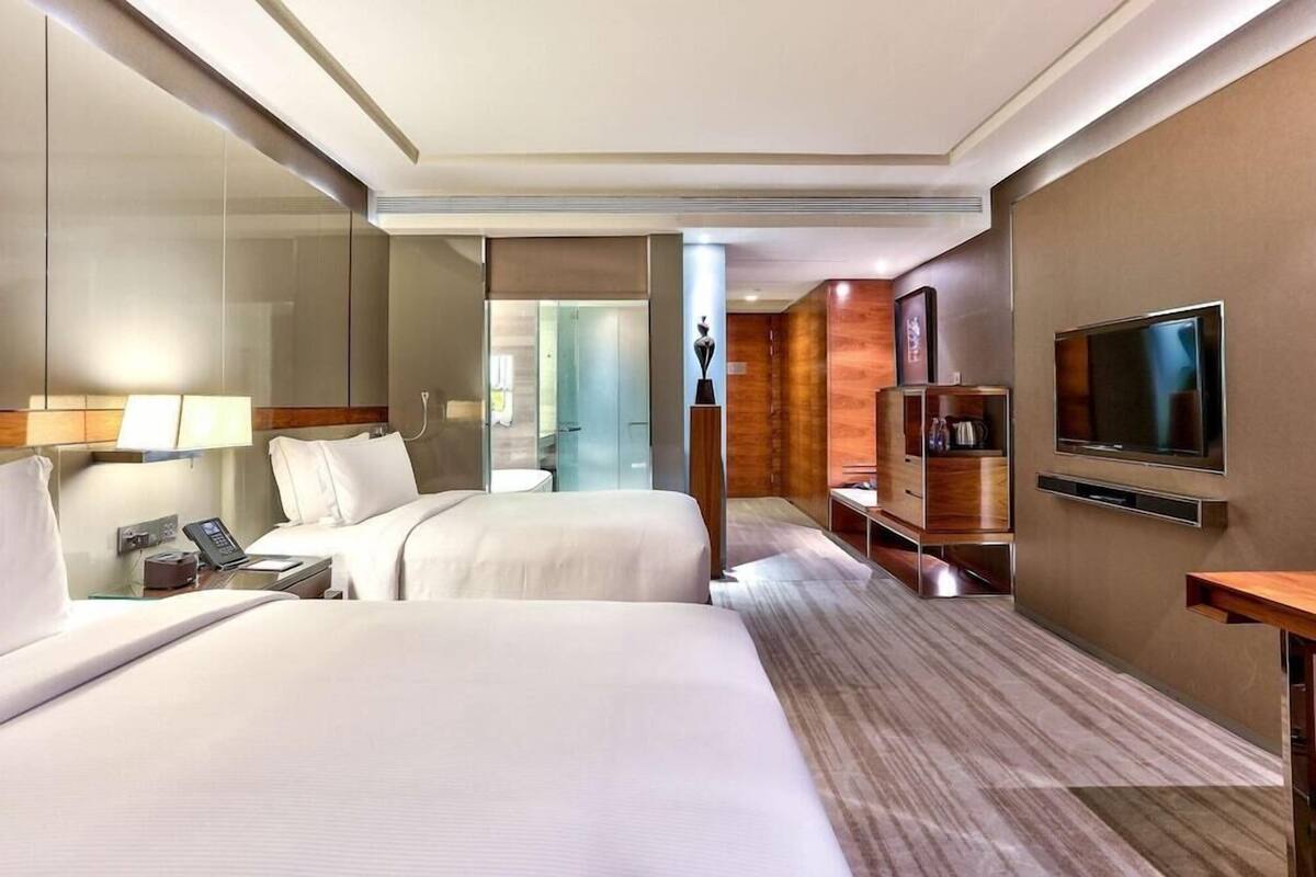 Une chambre d’hôtel avec deux lits, une télévision, un bureau avec un téléphone et une salle de bain visible à travers une porte en verre.