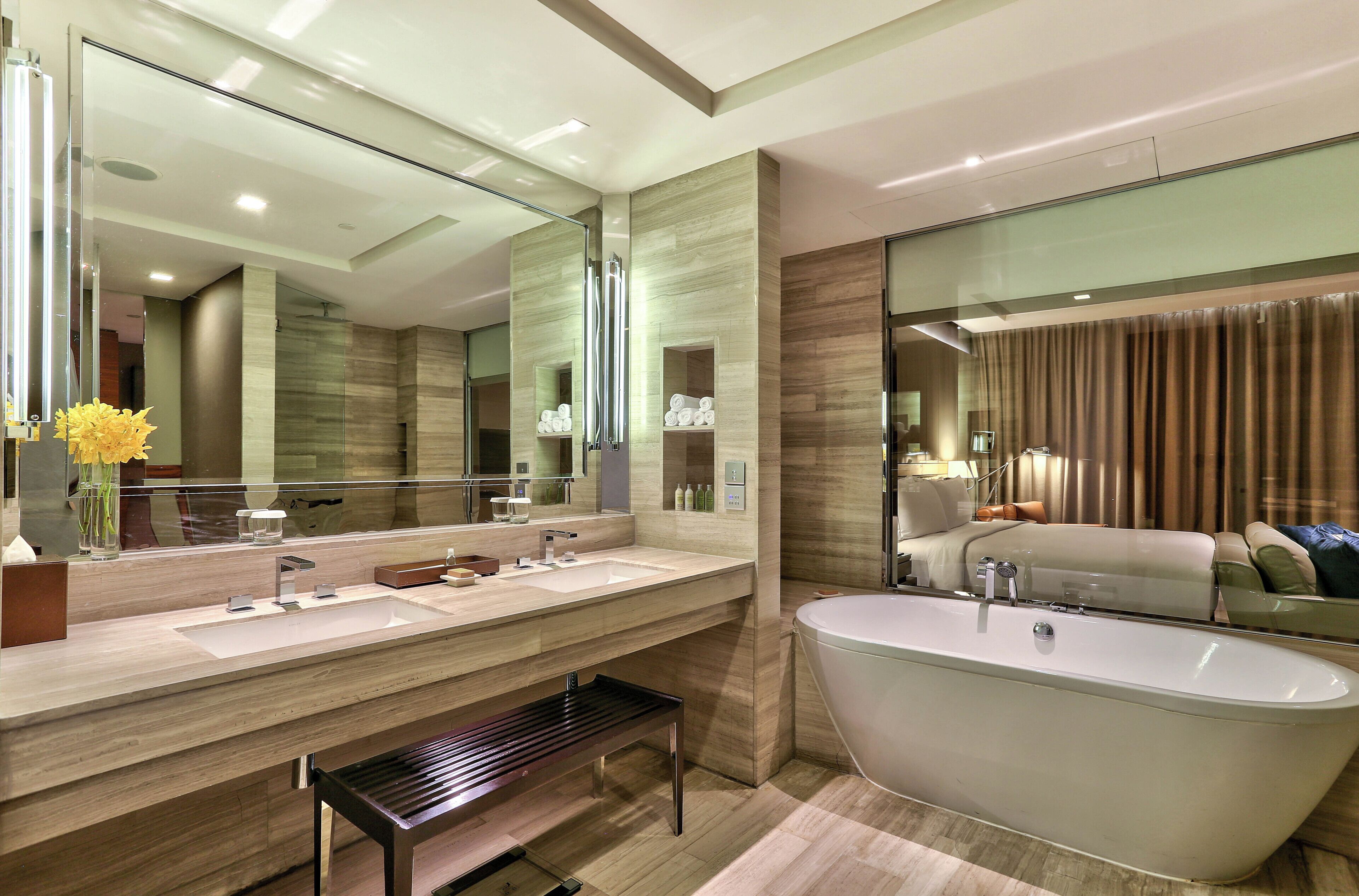 A modern bathroom with a freestanding bathtub, a large mirror, and a bench.