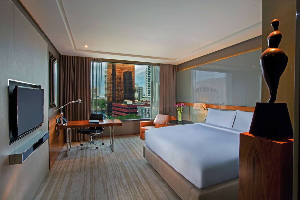 Une chambre d’hôtel dotée d’un grand lit, d’un bureau avec une chaise, d’une télévision et offrant une vue sur le paysage urbain grâce à de grandes fenêtres.
