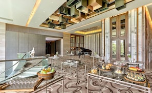 A spacious lobby with a grand piano, a glass staircase, and a buffet area with various food items.