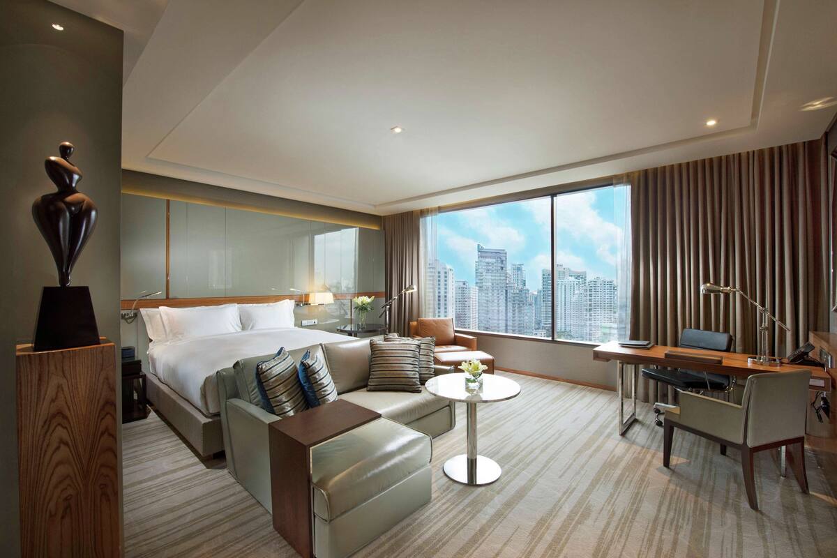 Une chambre d’hôtel équipée d’un lit, d’un canapé, d’un bureau et d’une grande fenêtre donnant sur la ville.