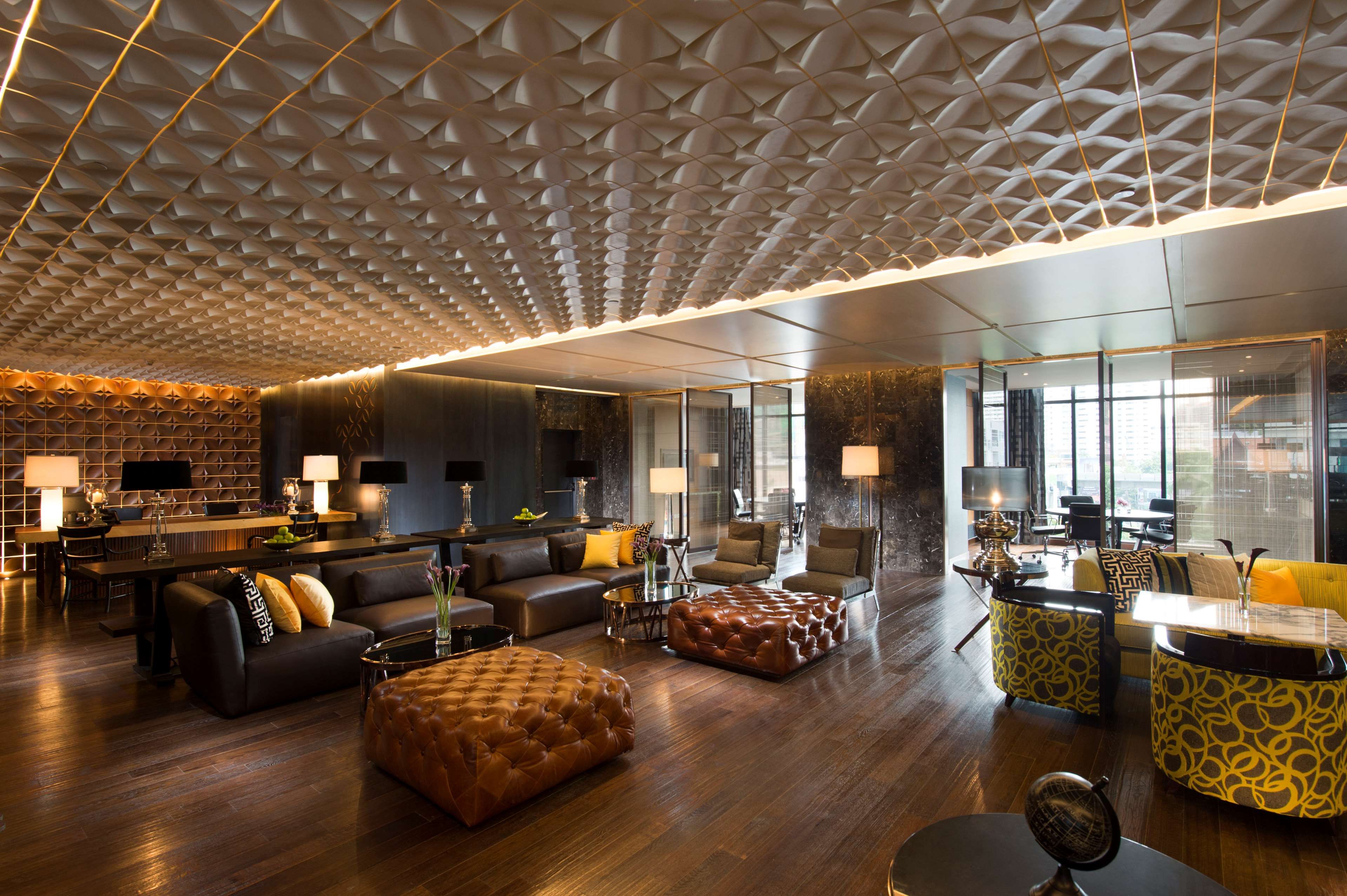 A modern hotel lobby with a geometric ceiling design, leather sofas, and a bar area.