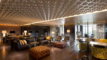 A modern hotel lobby with a geometric ceiling design, leather sofas, and a bar area.
