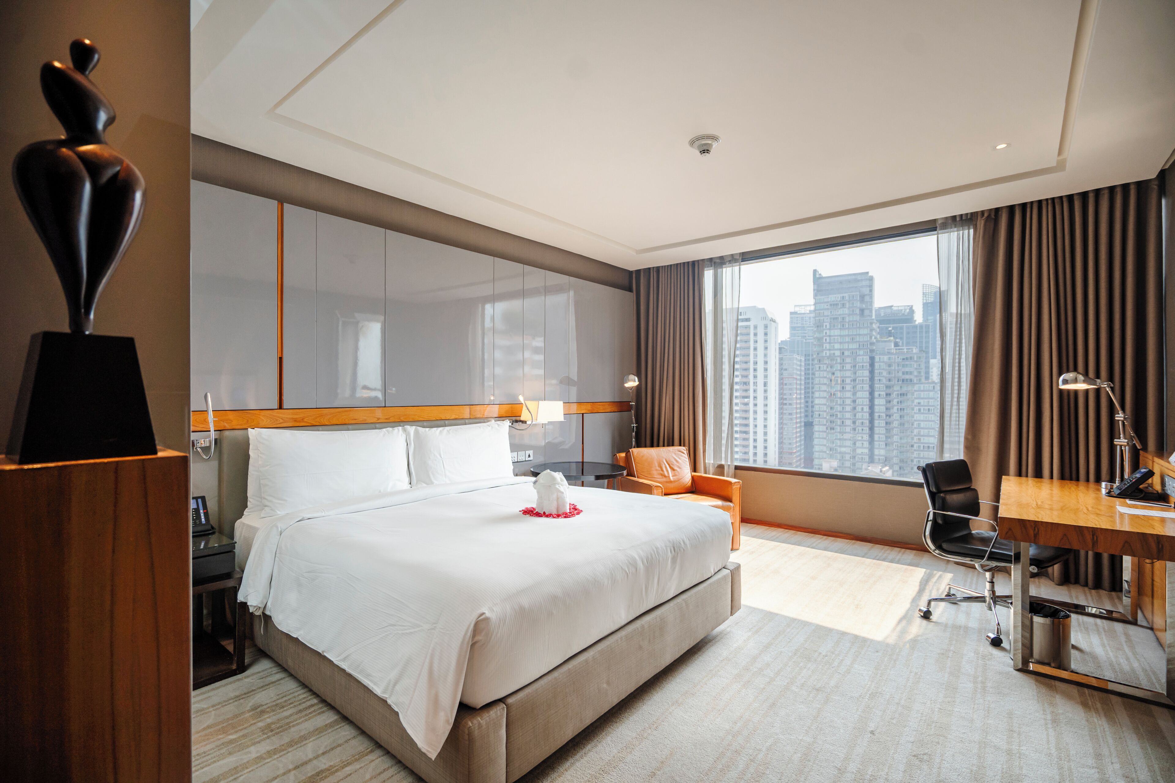 A hotel room with a large bed, a desk, a chair, and a view of the cityscape.