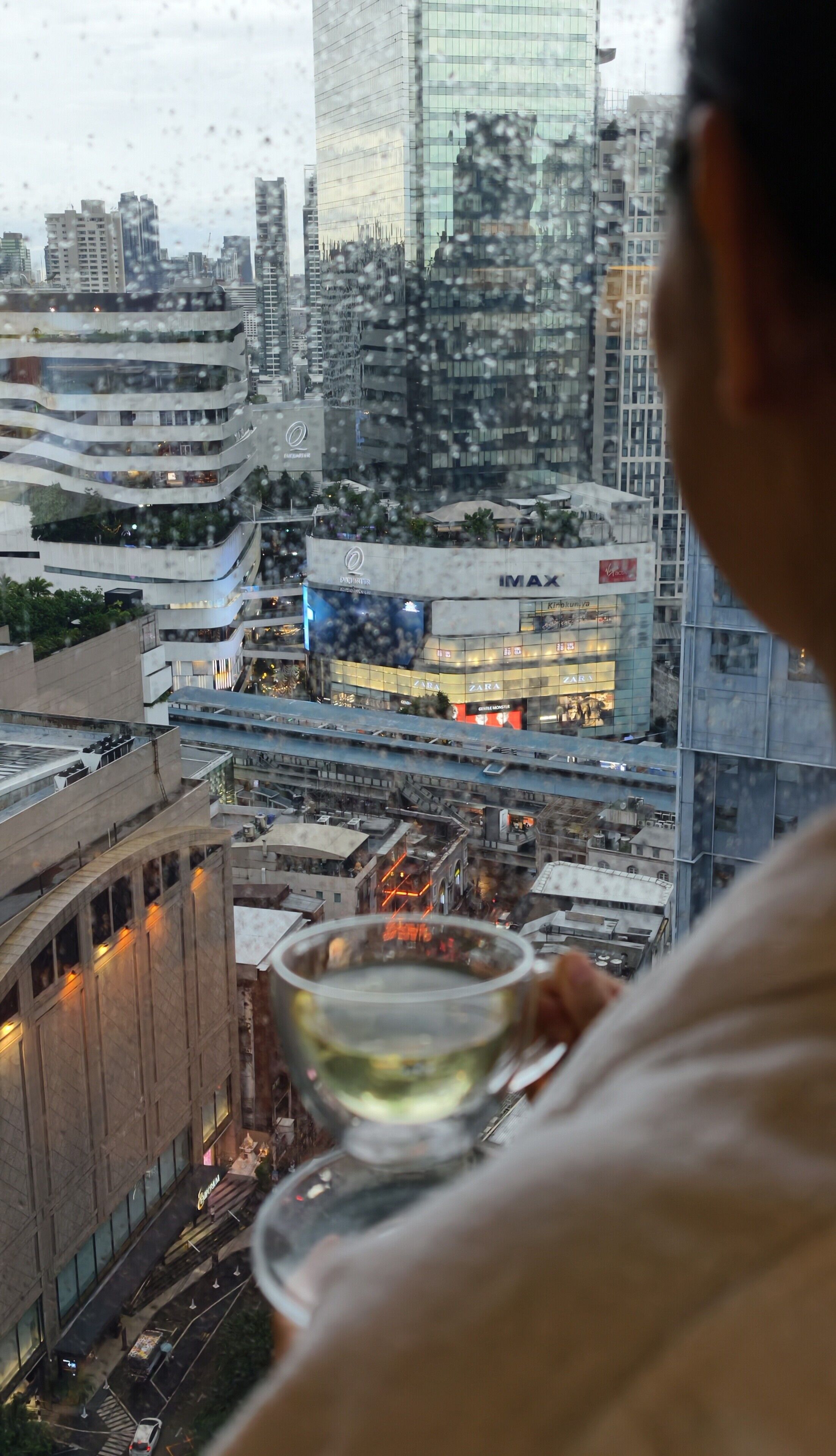 A cityscape with modern buildings, including a Zara store, and a person holding a glass.