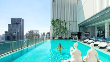 A rooftop pool with a city view, lounge chairs, and a seating area with a white statue.
