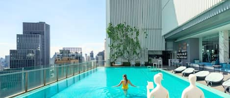 Piscina en la azotea con vistas a la ciudad, sillones de descanso y un espacio de estar con una estatua blanca.