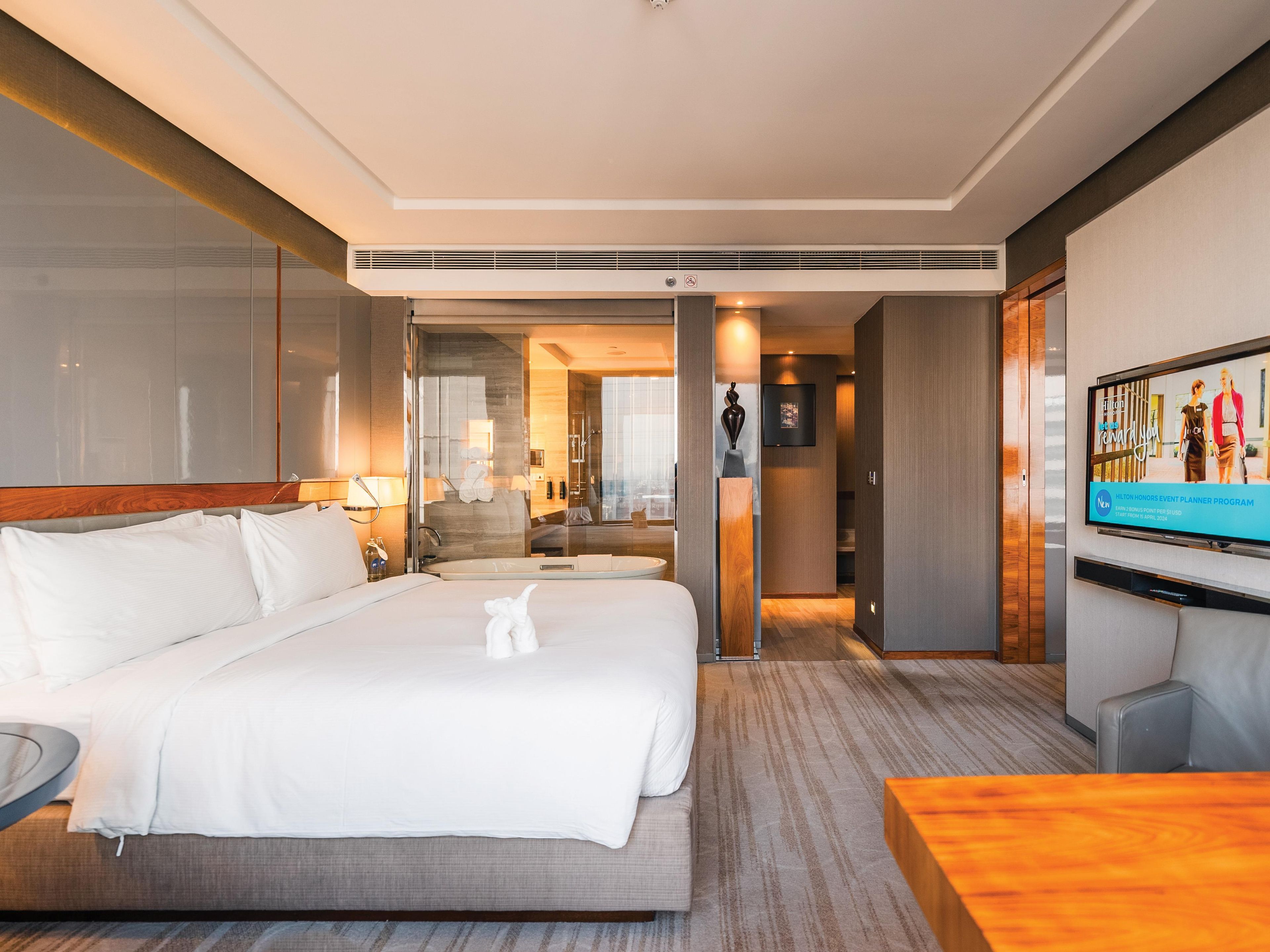 A hotel room with a large bed, a desk, a TV, and a bathroom visible through an open door.