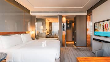 A hotel room with a large bed, a desk, a TV, and a bathroom visible through an open door.
