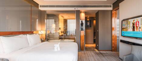 Habitación de hotel con una cama grande, un escritorio, un televisor y un baño visible a través de una puerta abierta.