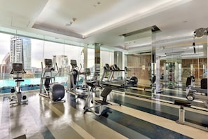 A modern gym with various exercise equipment, large windows, and a city view.