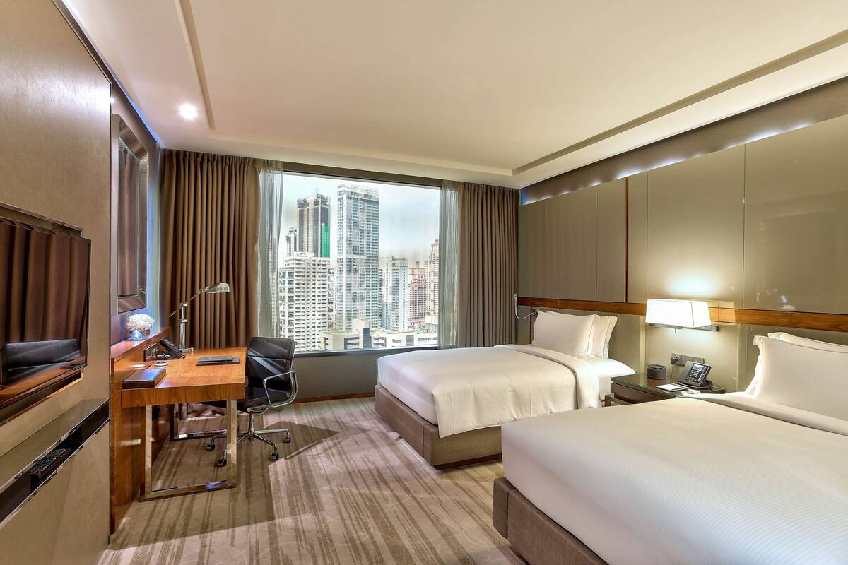 Une chambre d’hôtel équipée d’un lit, d’un bureau, d’une chaise et d’une grande fenêtre donnant sur la ville.