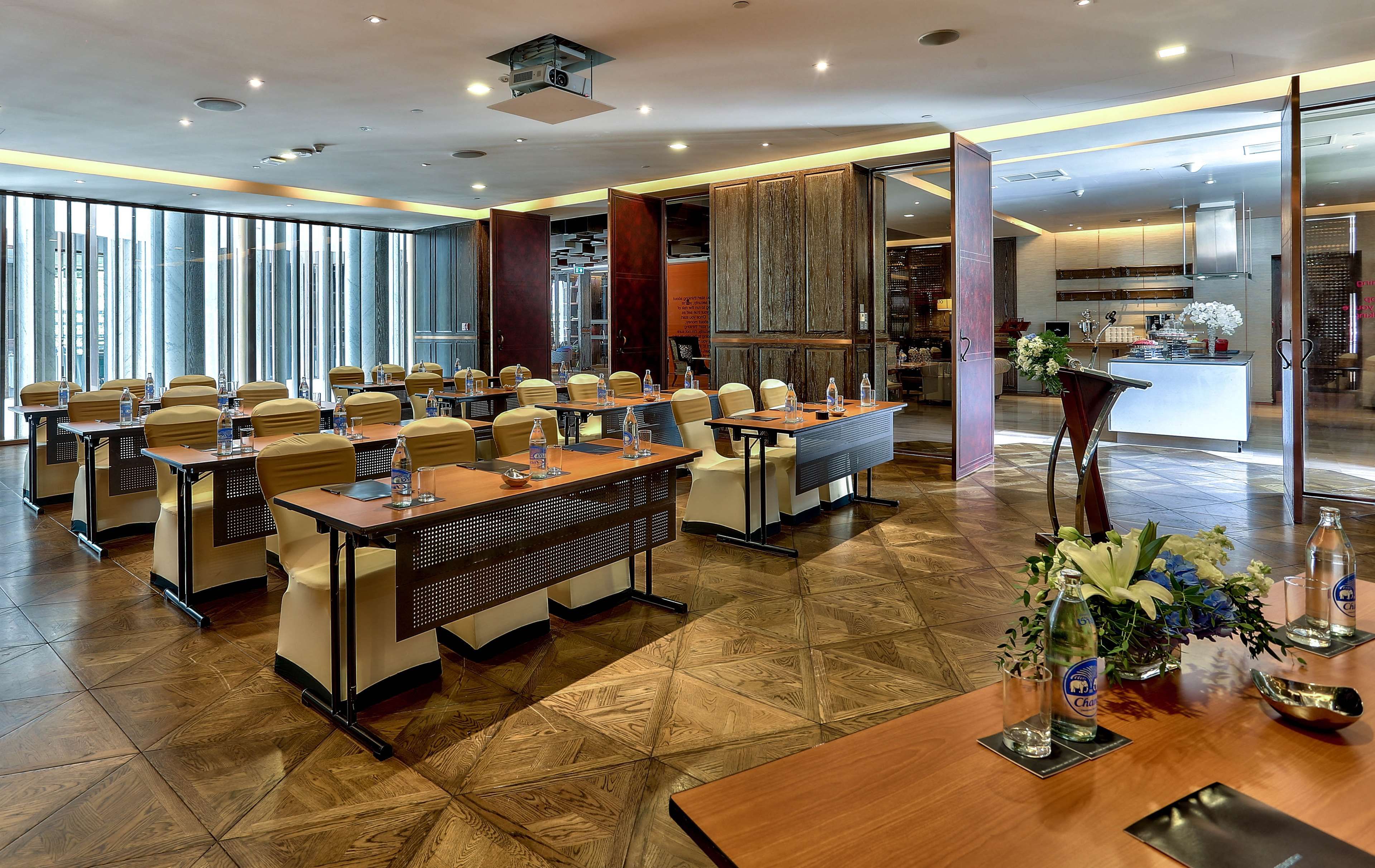 A conference room with tables and chairs, a kitchen area, and a large window with a view.