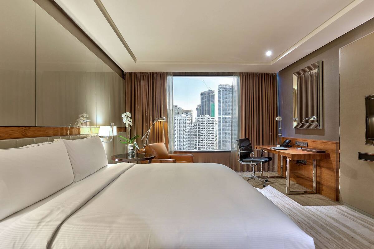 Une chambre d’hôtel avec un grand lit, un bureau, une chaise et une vue sur de hauts immeubles.