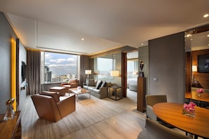 A modern hotel room with a city view, a sitting area with a sofa and chairs, a dining table, and a separate bedroom area.