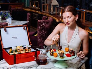 Una mujer sentada a una mesa con diversos postres y una tetera.